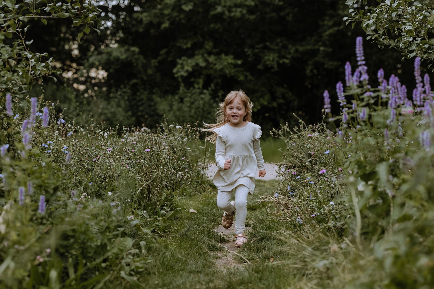 A child runs joyfully through a summer garden filled with purple lupines and white wildflowers.