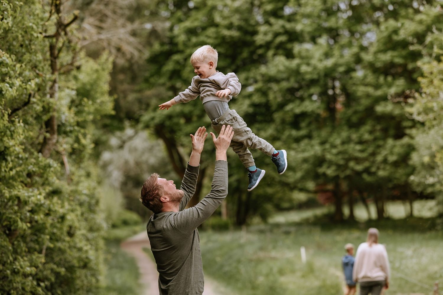 A playful moment captured in a lush garden setting as someone lifts a small child high into the air.
