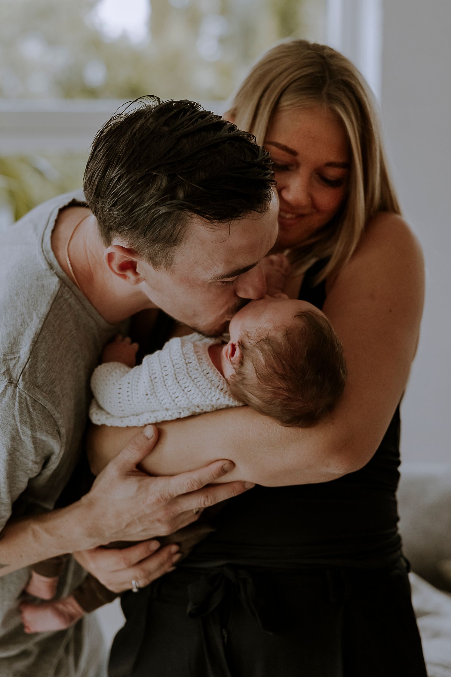 New parents sharing an intimate moment with their newborn baby dressed in white knit clothing.