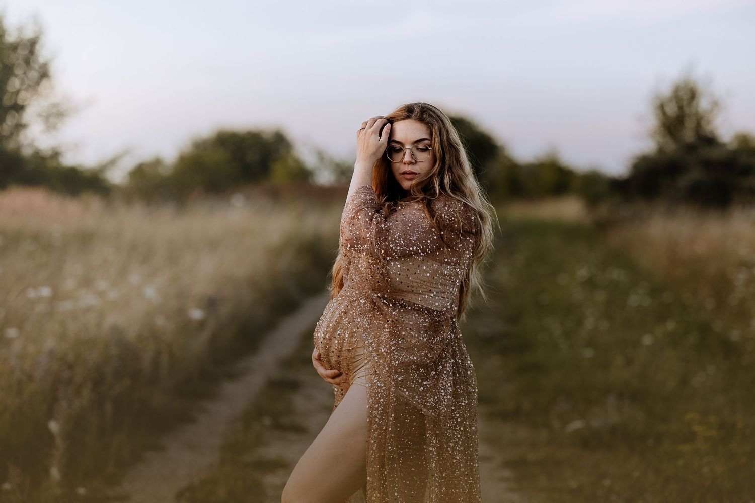 A person in a sparkly gold dress stands in a sunlit field during golden hour.