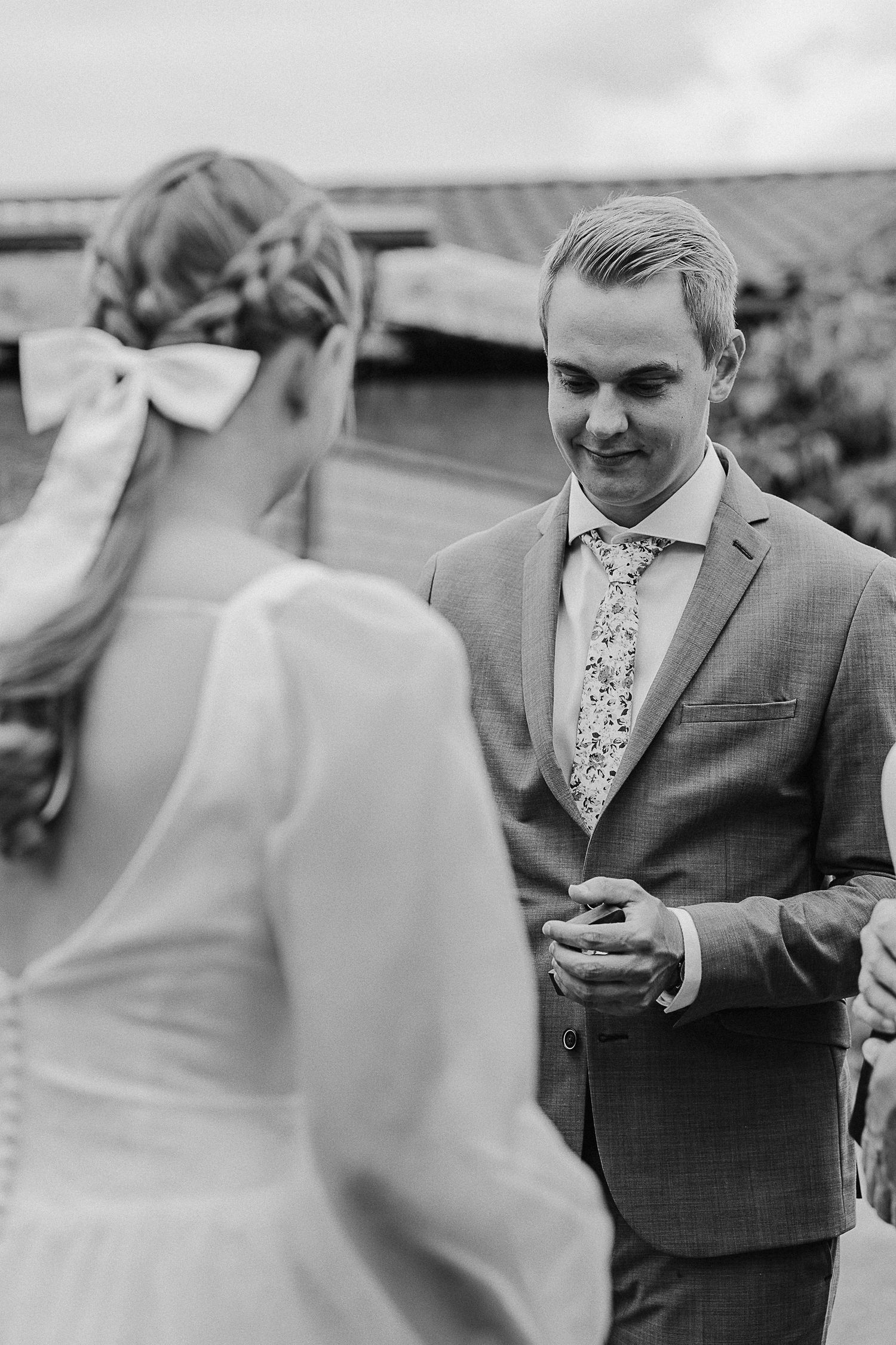 A close-up black and white photo of a wedding couple exchanging rings during an outdoor ceremony.