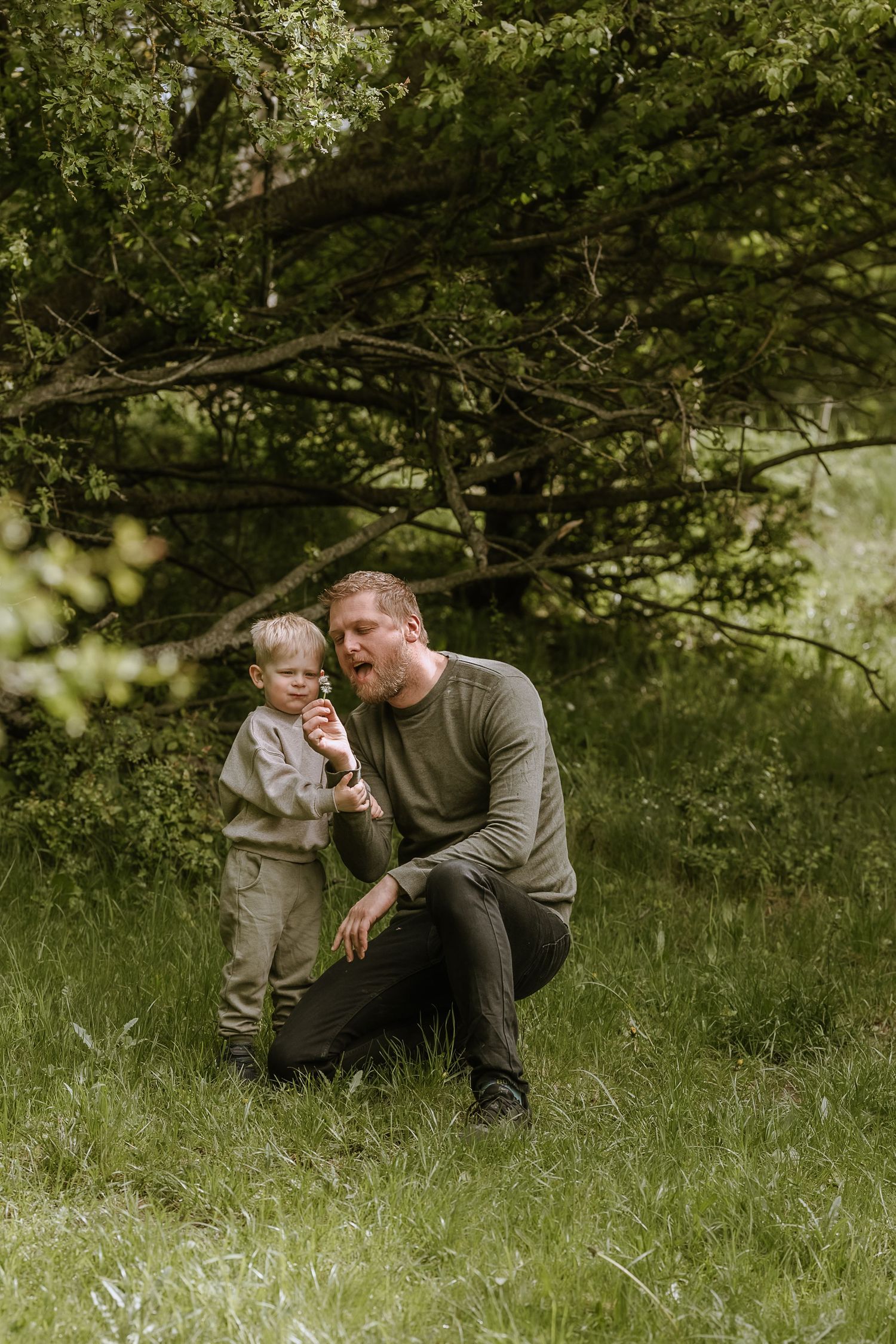 A touching outdoor moment under green trees as a small child and adult in gray share a special moment in nature.