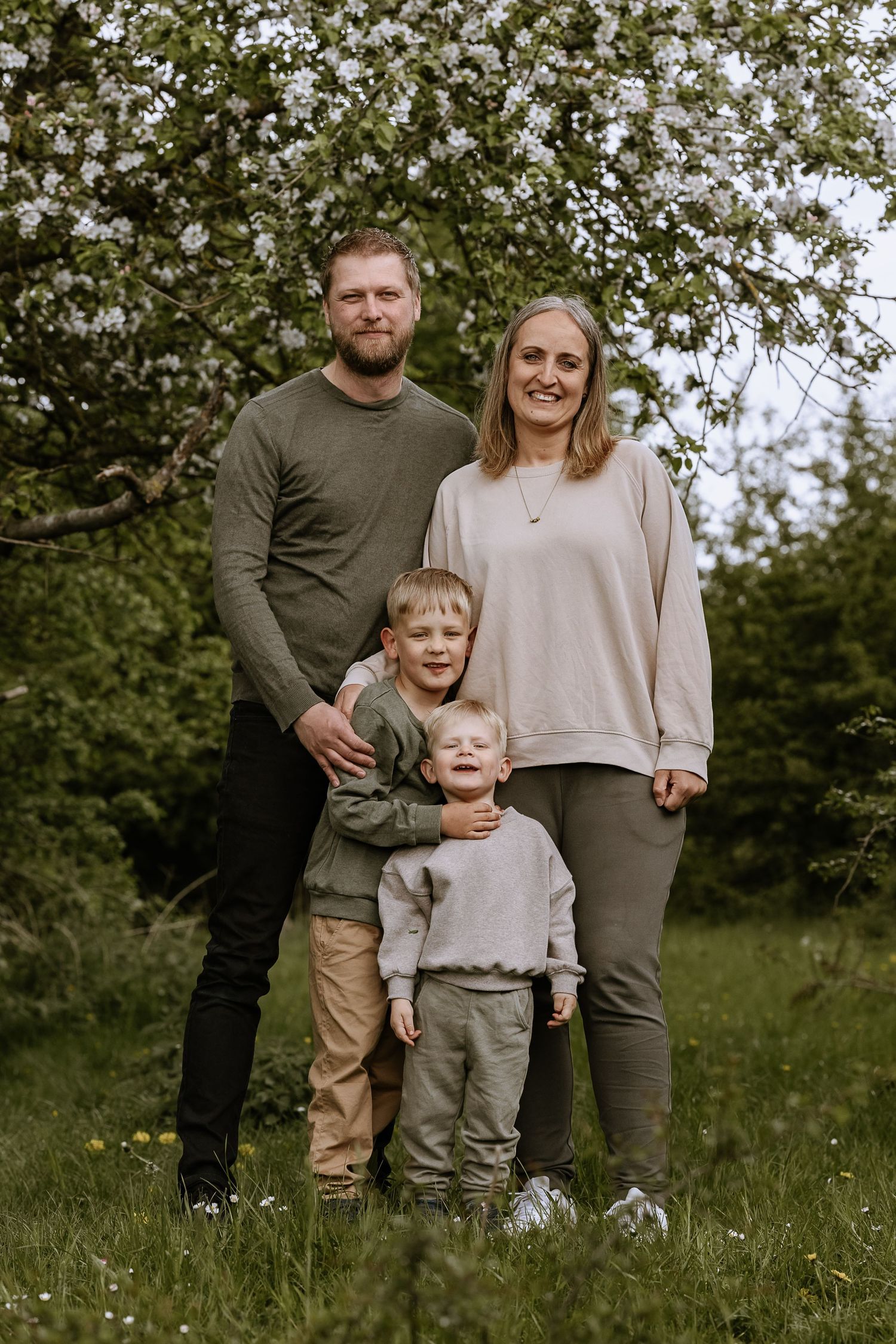 Family portrait with two young children standing in spring garden with blooming tree.