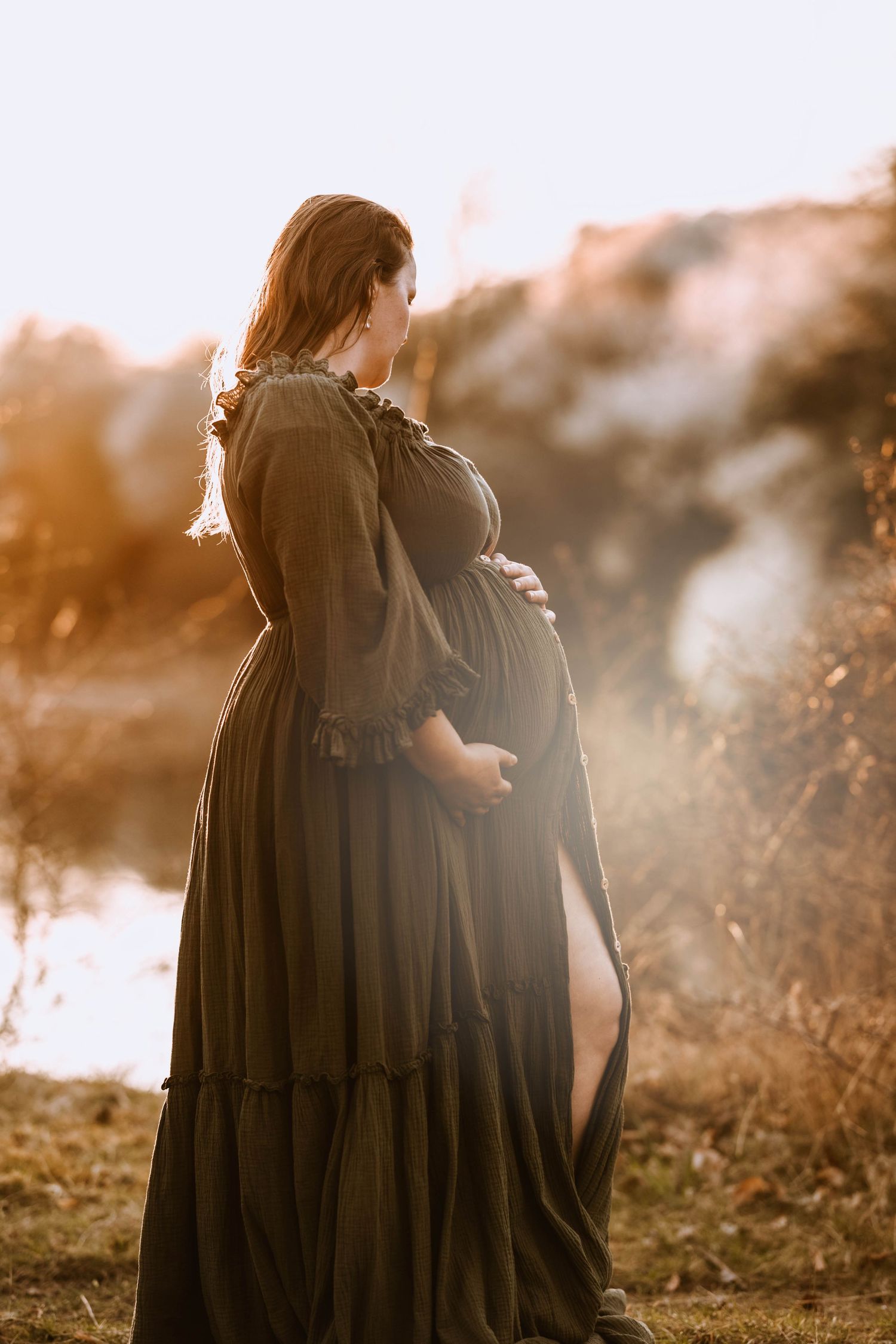 Atmospheric side view maternity portrait with warm sunset lighting and flowing dress.