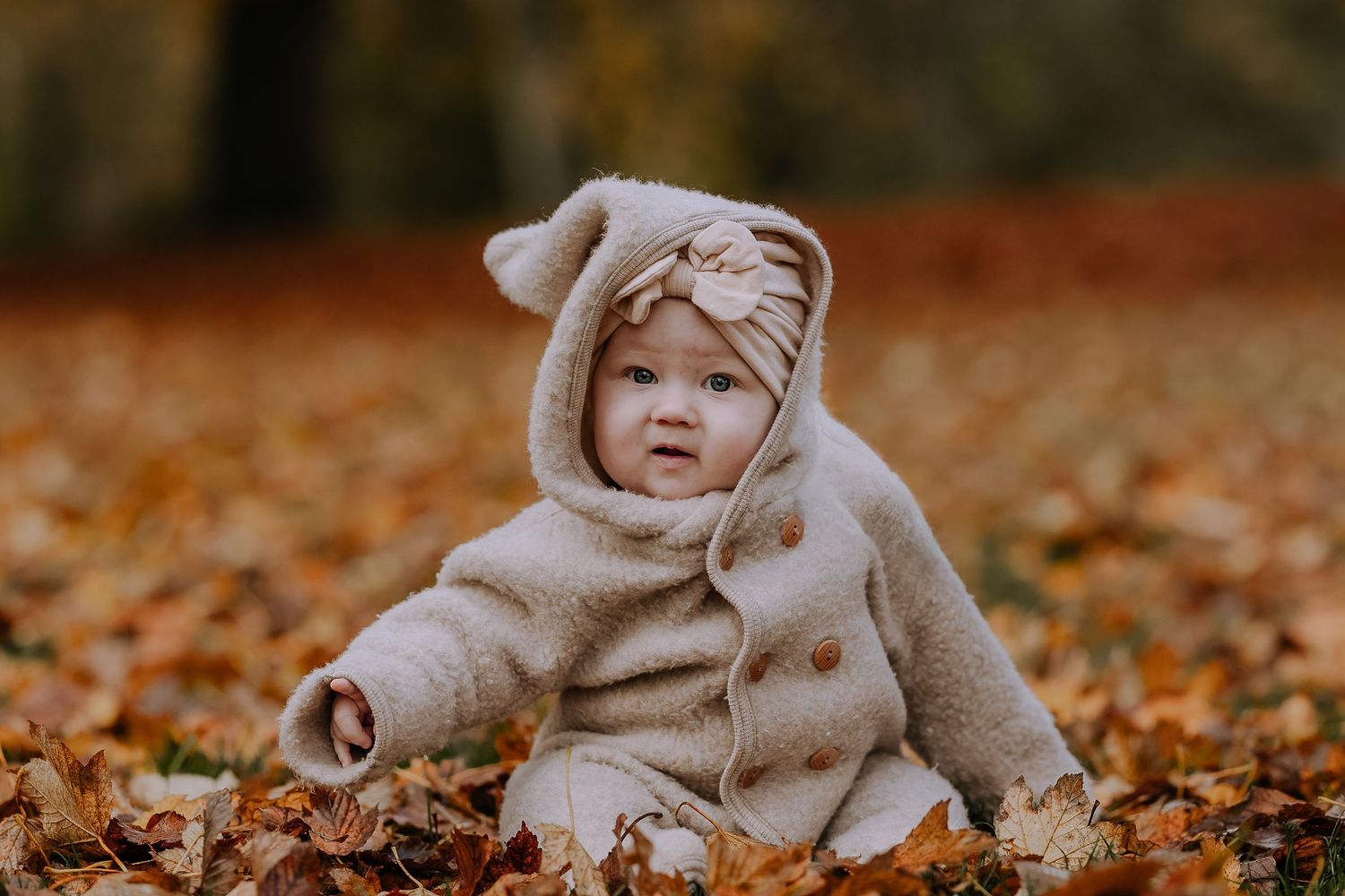 A child in a cozy beige bear costume plays in a pile of vibrant autumn leaves during fall.