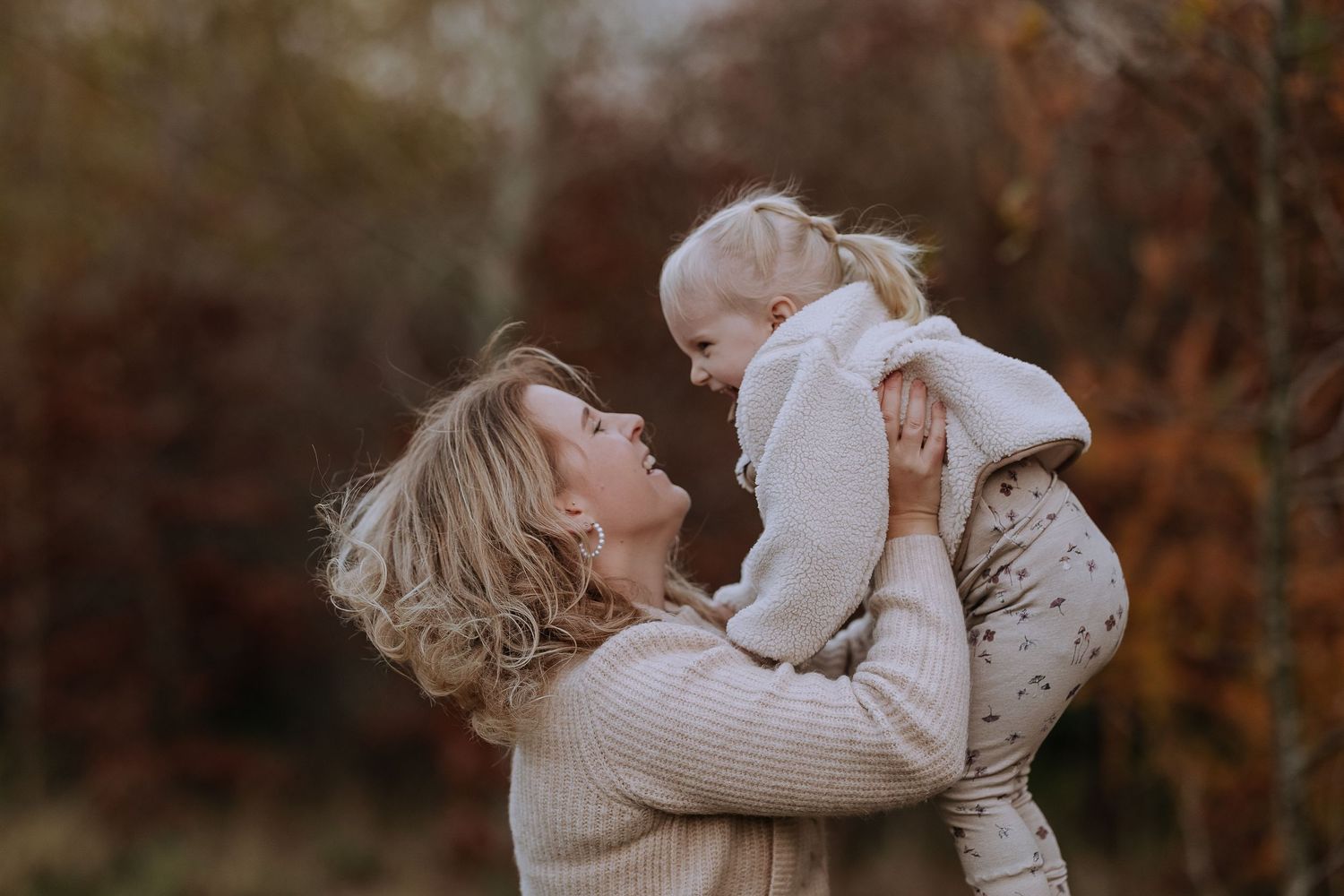 Parent and child share a tender moment together in an autumn setting wearing cozy sweaters.