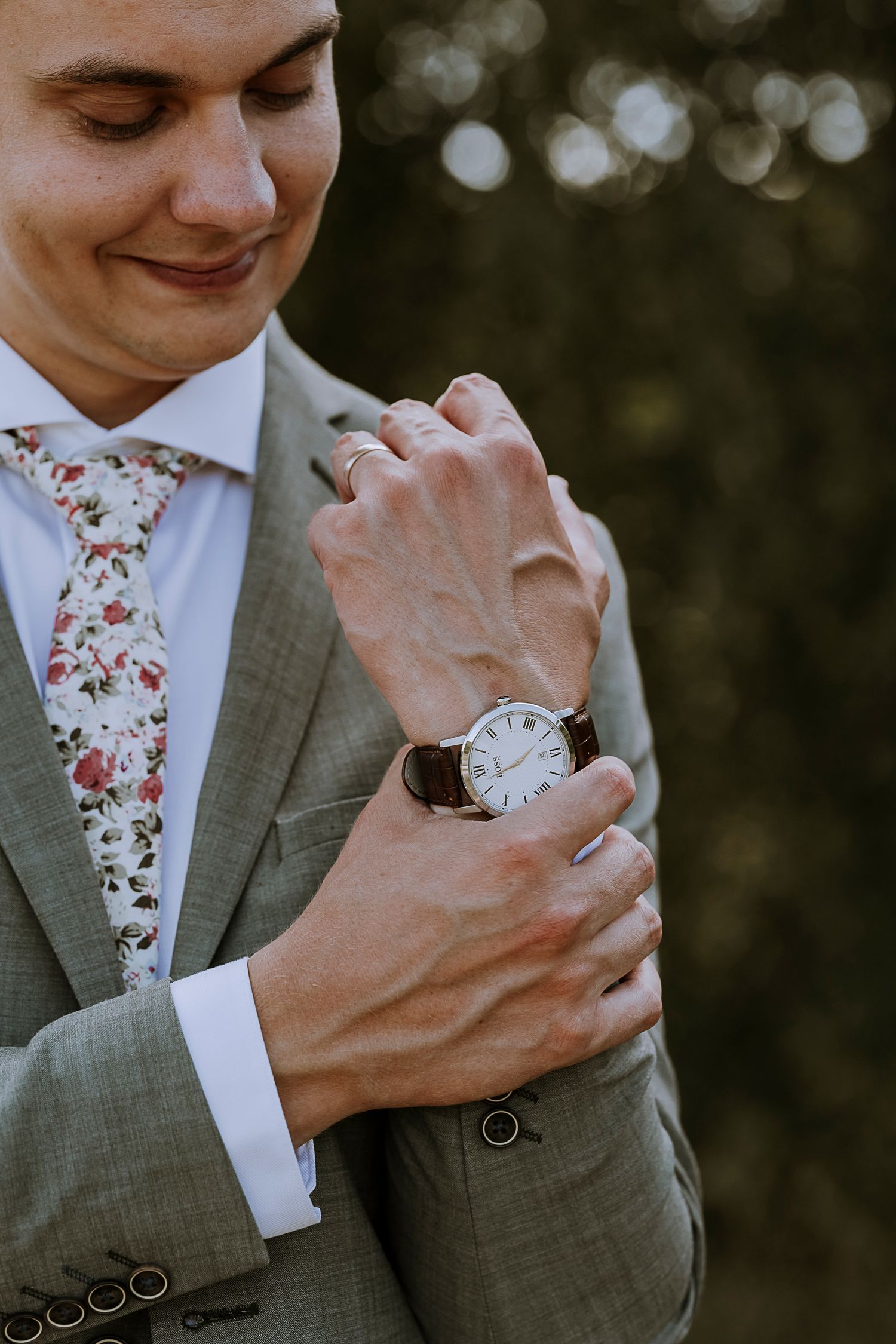 Close-up of a person in a floral tie and grey suit adjusting their watch.