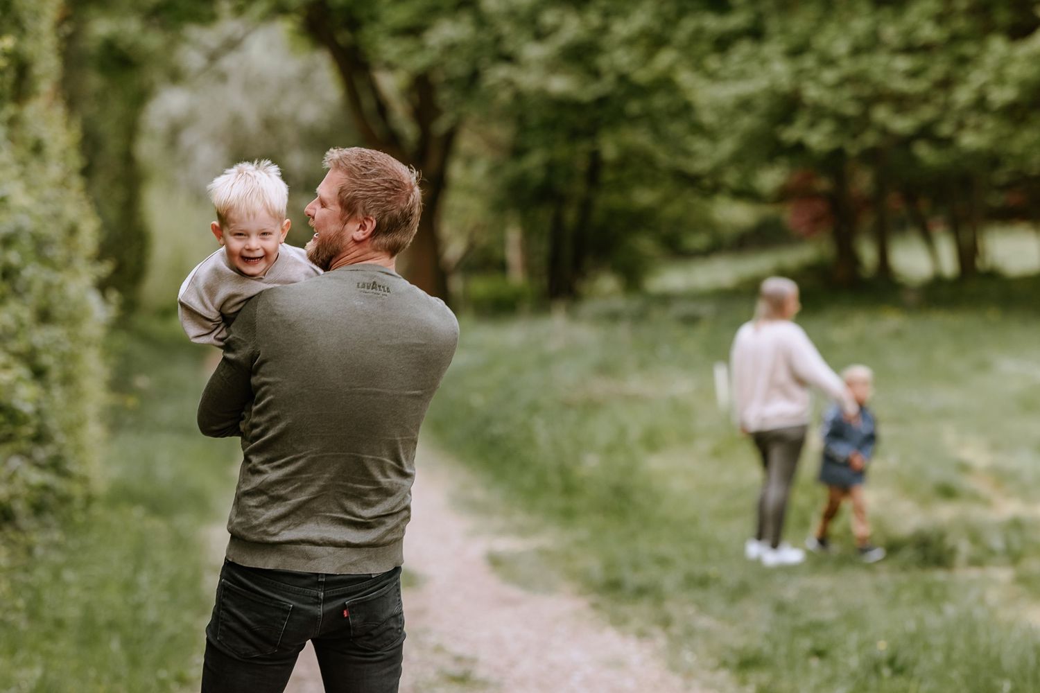 Family moment captured on a wooded path with people walking in the background.