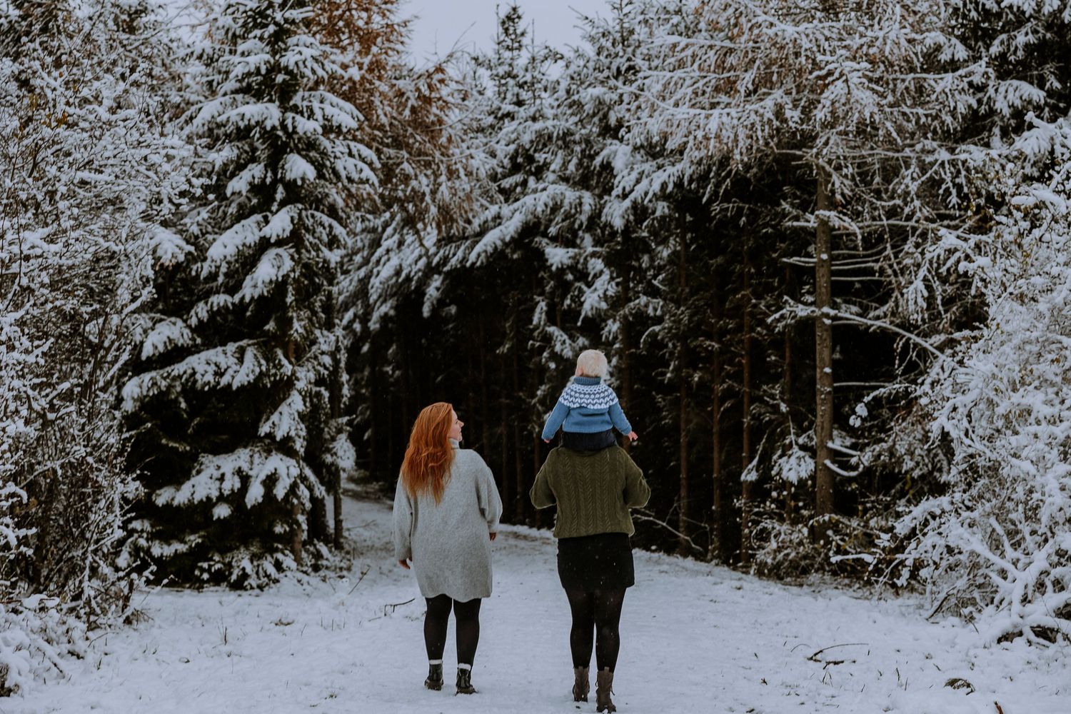 Two people walking hand in hand on a snowy forest path.