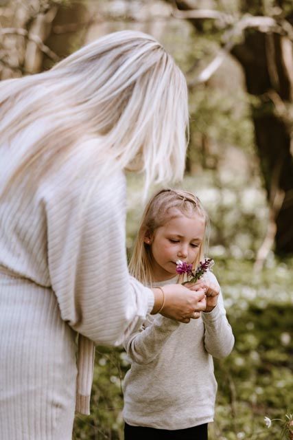 A gentle moment in nature as a small child in a beige sweater delicately holds and observes a butterfly in a garden setting.