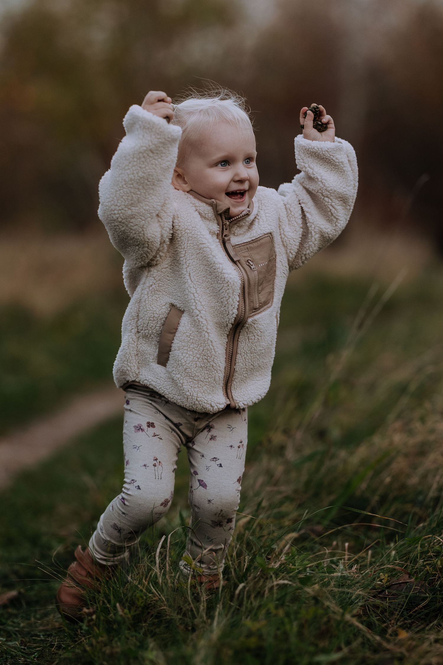 Baby in white fleece outfit crawls and plays on grass during a fall outdoor photo session.
