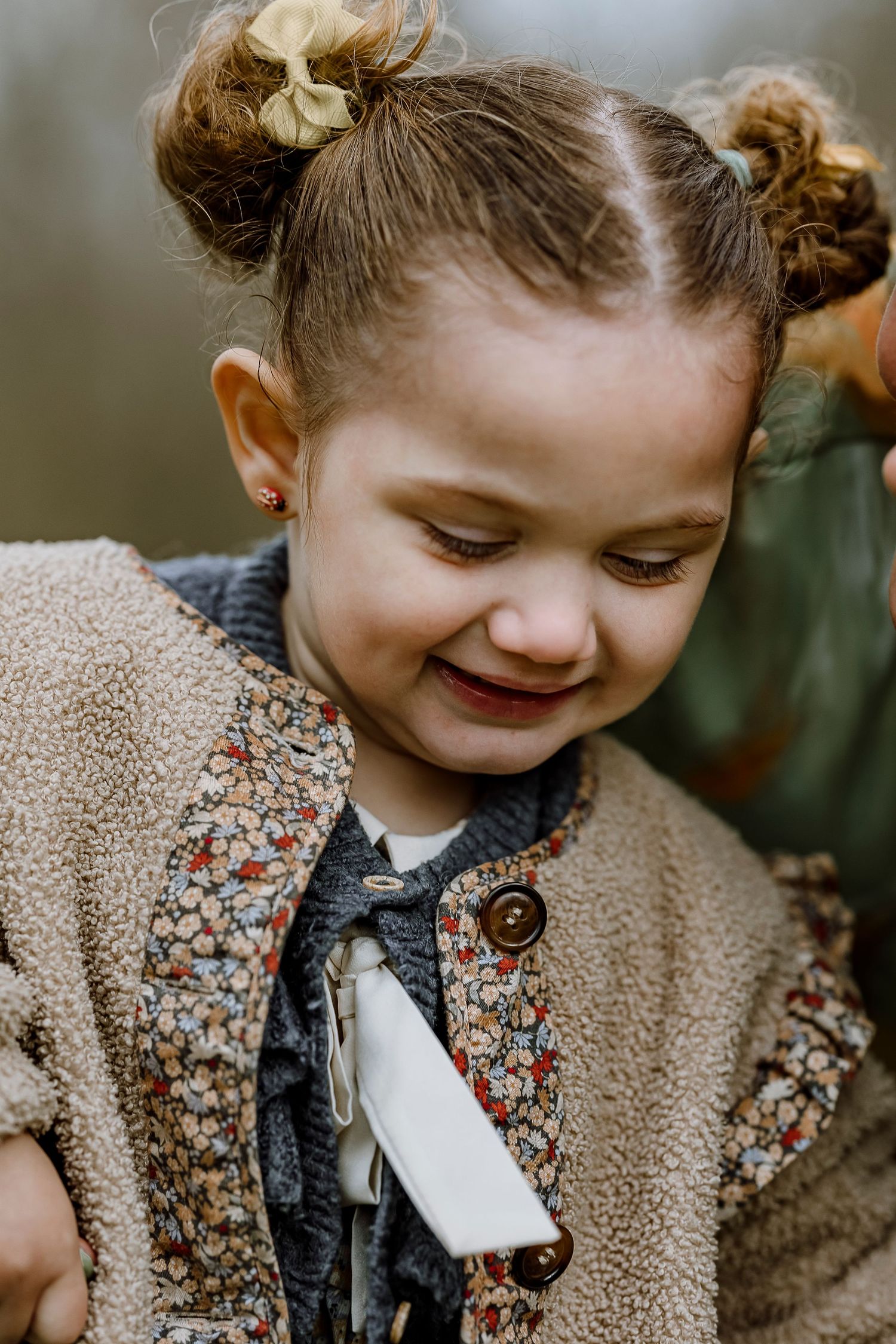 A child in a floral dress and beige cardigan smiles while looking down in a series of candid outdoor portrait shots.