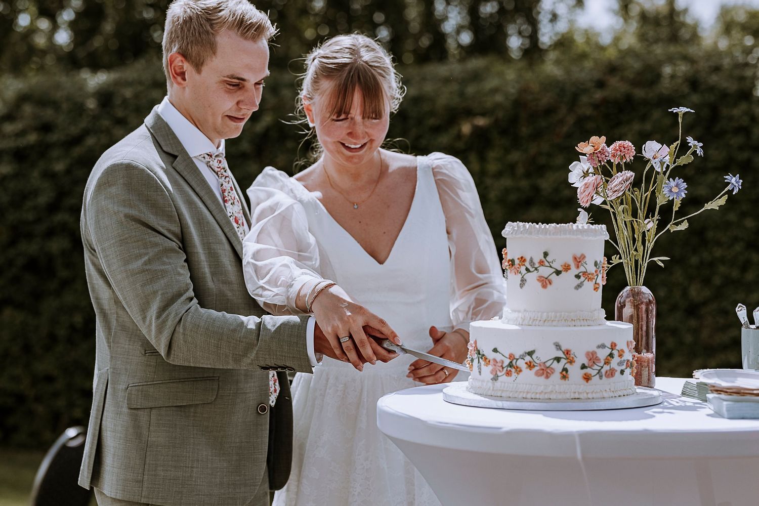 Couple cutting elegant three-tier wedding cake decorated with floral details.