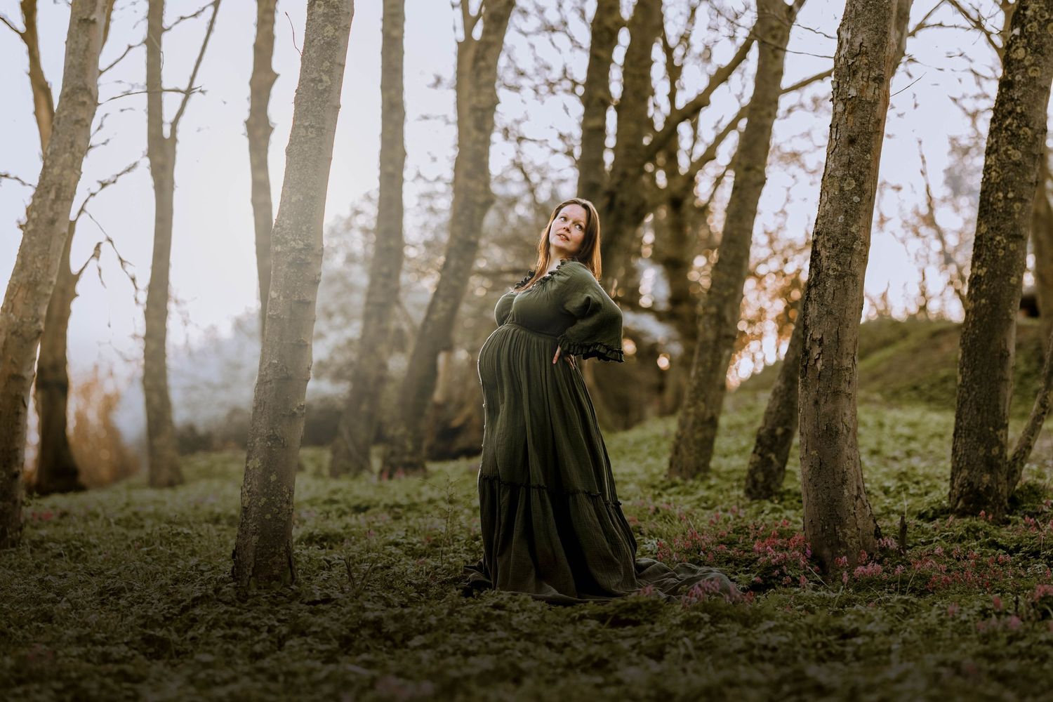 Artistic maternity portrait in a dark flowing dress against a misty woodland backdrop.