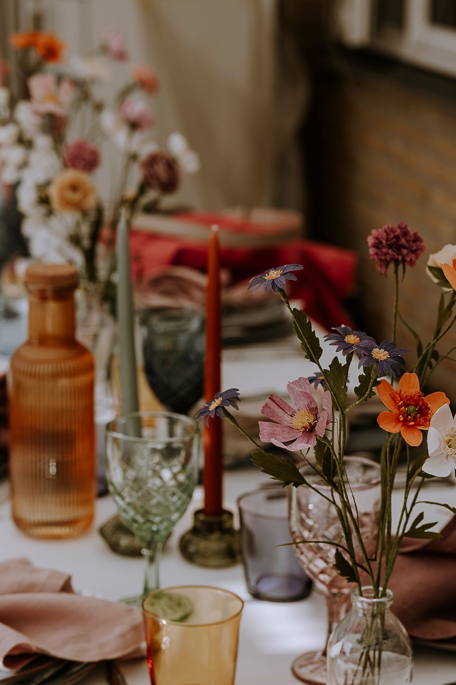 Romantic table setting with amber bottles, red candles, and wildflowers in vintage glassware.