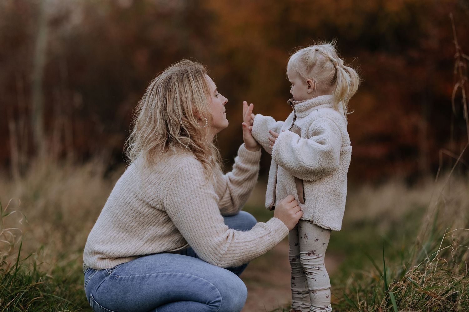A tender outdoor moment between parent and child wearing matching beige sweaters in an autumn field.