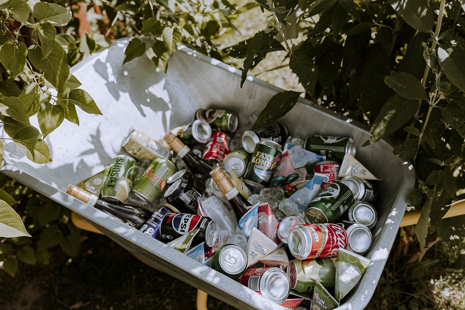 Ice-filled wheelbarrow stocked with assorted beverages and drinks at outdoor event.