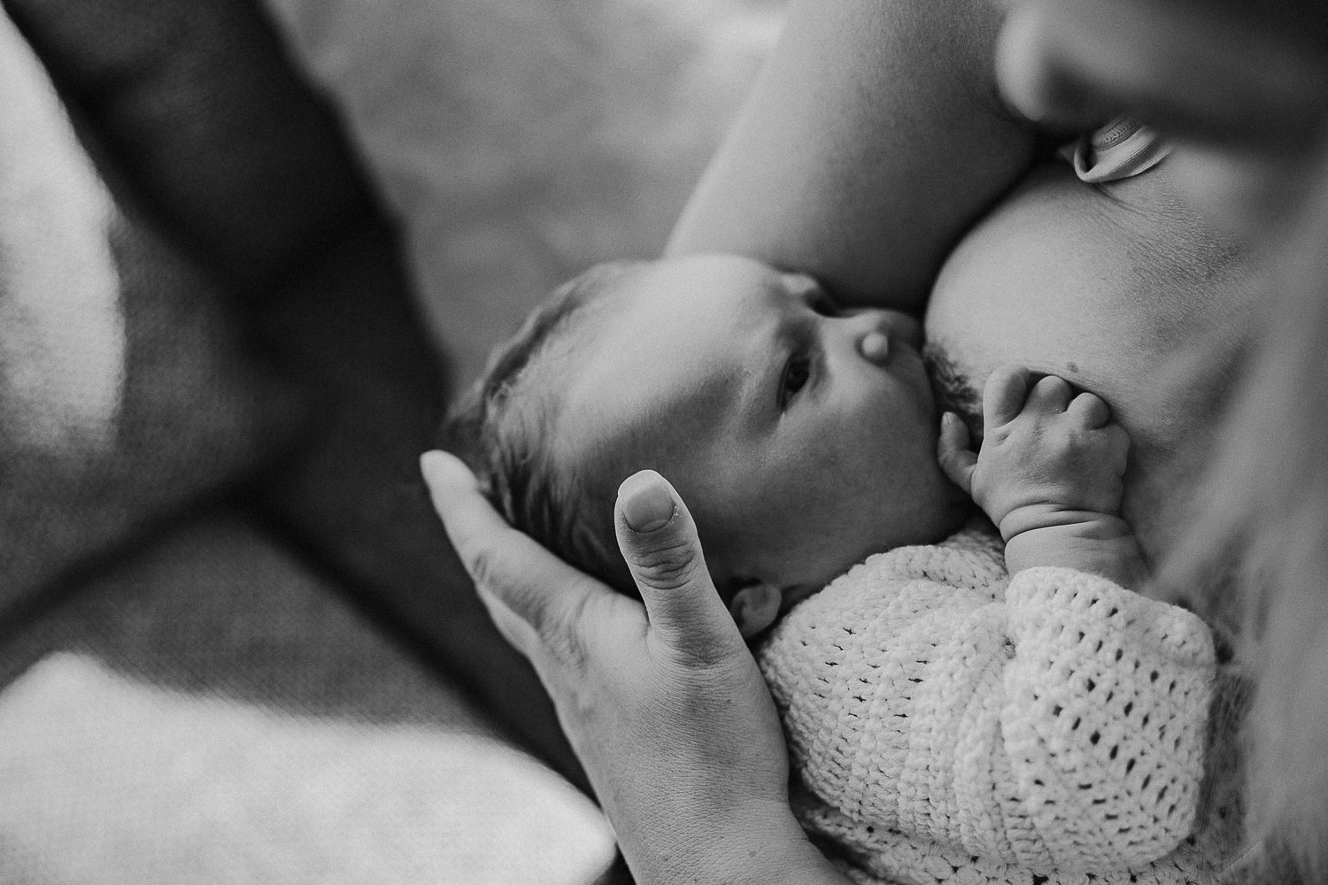 Black and white intimate portrait of nursing newborn in tender embrace.