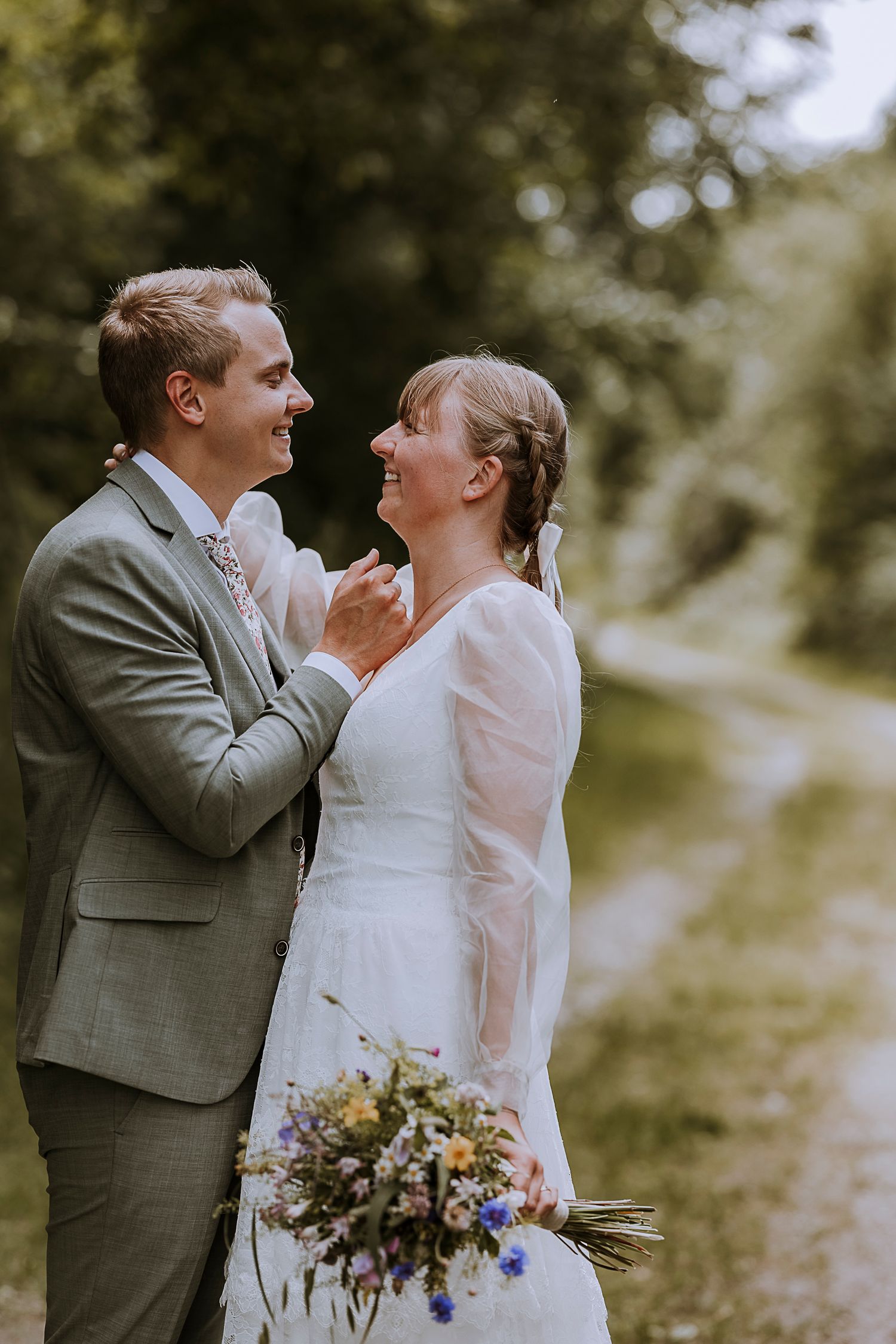 Joyful wedding couple sharing intimate moment with bouquet in woods.