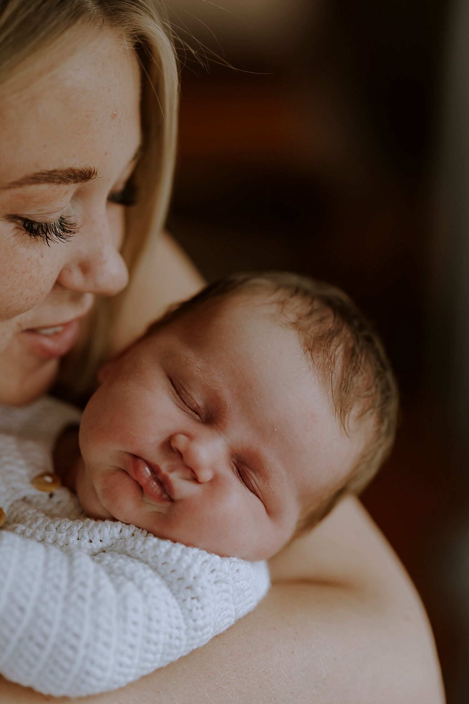 Intimate portrait of parent snuggling with sleeping newborn in white sweater.