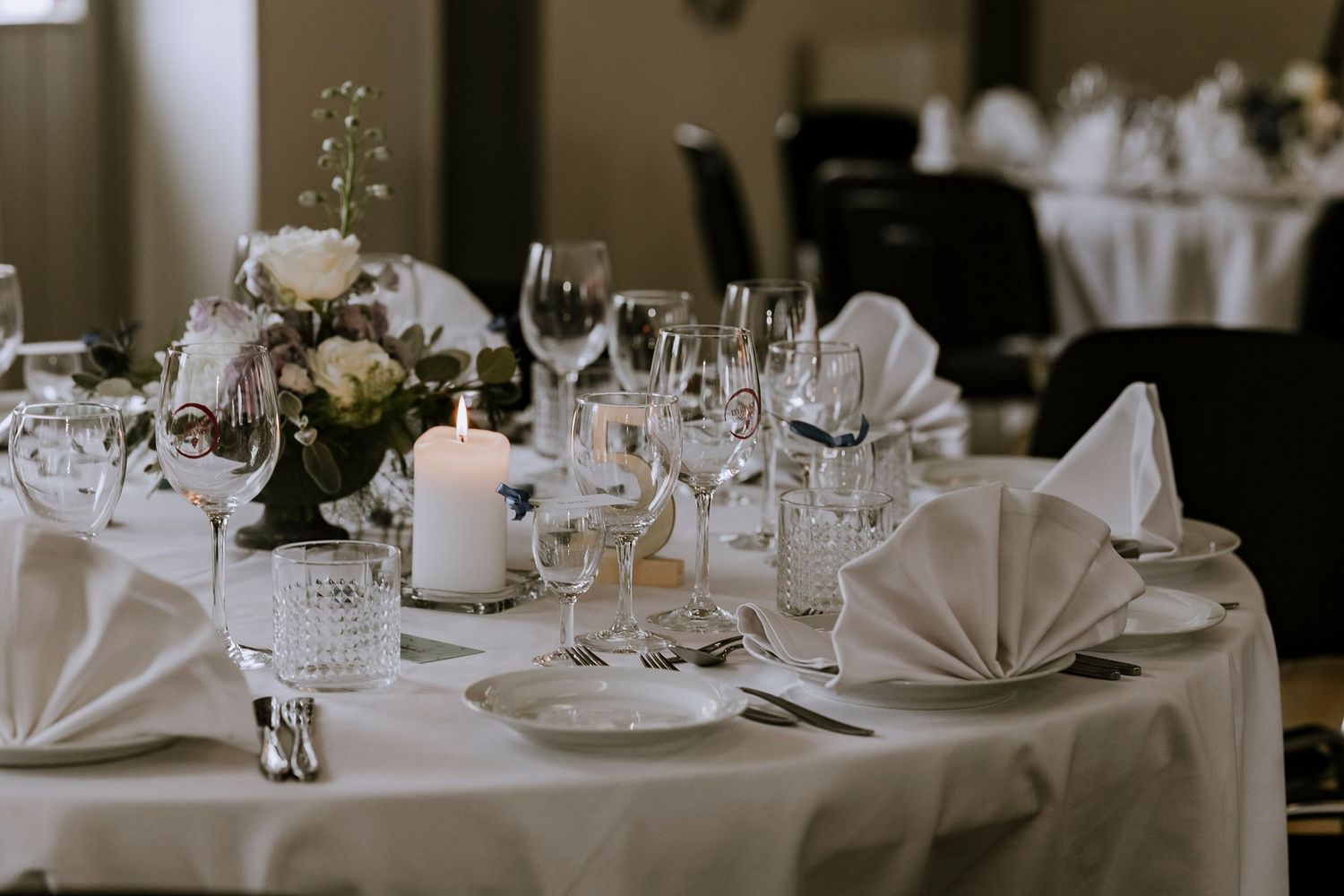 Elegant wedding reception table setting with folded white napkins, wine glasses, and floral centerpiece with candle.