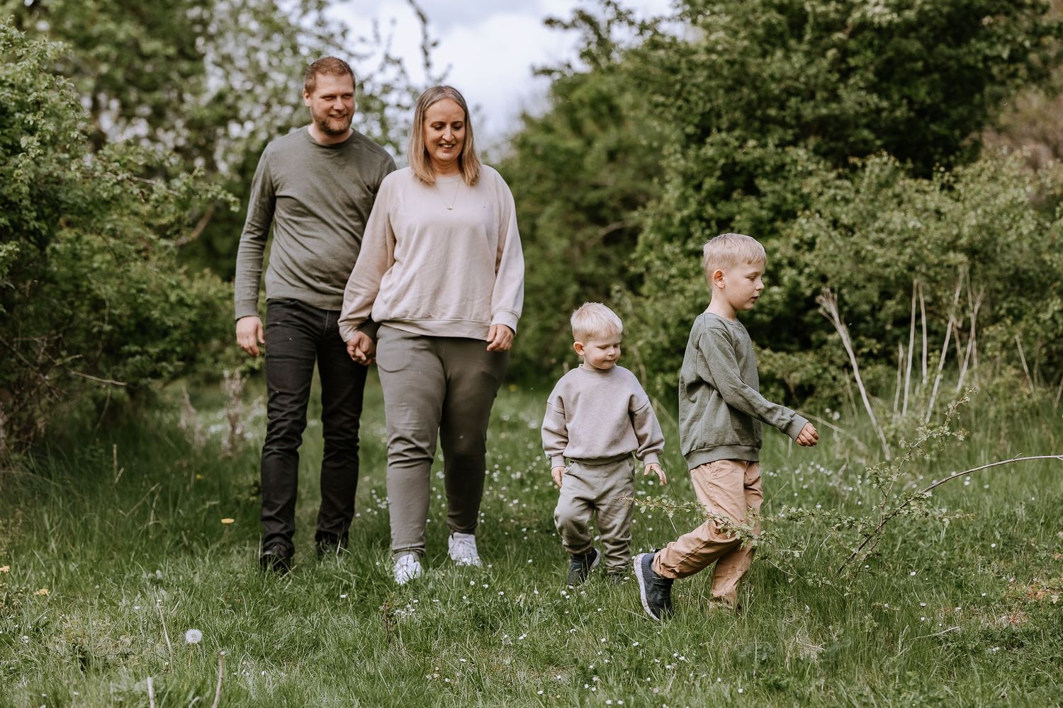 A family of four walking together through a green spring meadow with children running ahead.