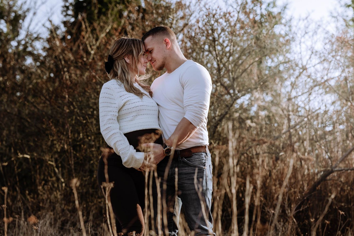Romantic couple embraces in a sunlit forest setting during an outdoor photo session.