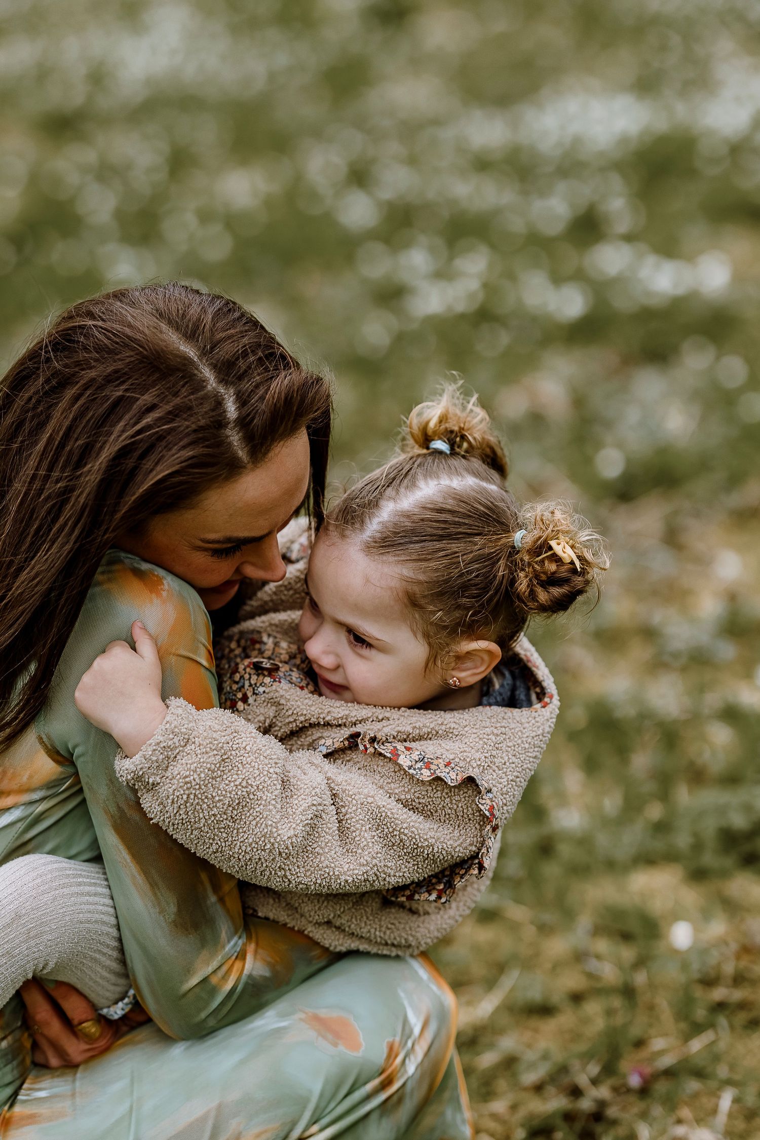 A tender moment between parent and child sharing an embrace outdoors in a natural setting with bokeh background.