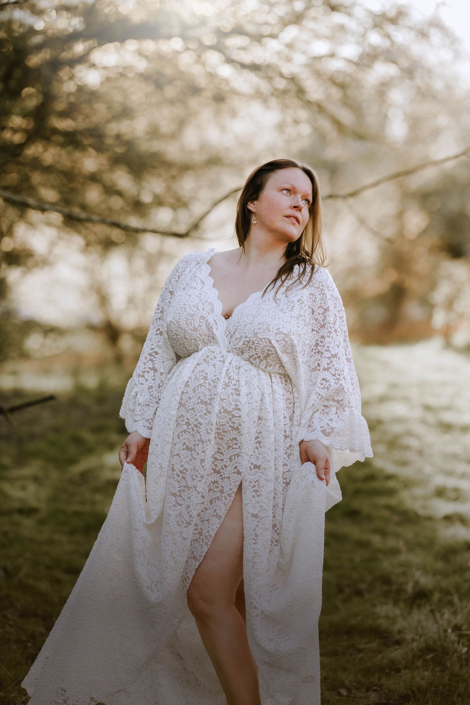 Beautiful maternity portrait with woman in white lace dress against golden sunset light.