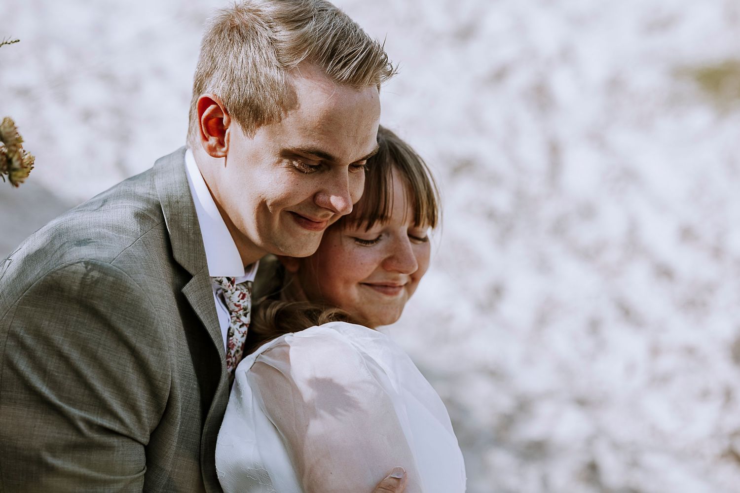 Joyful wedding portrait capturing a close embrace against a light background.
