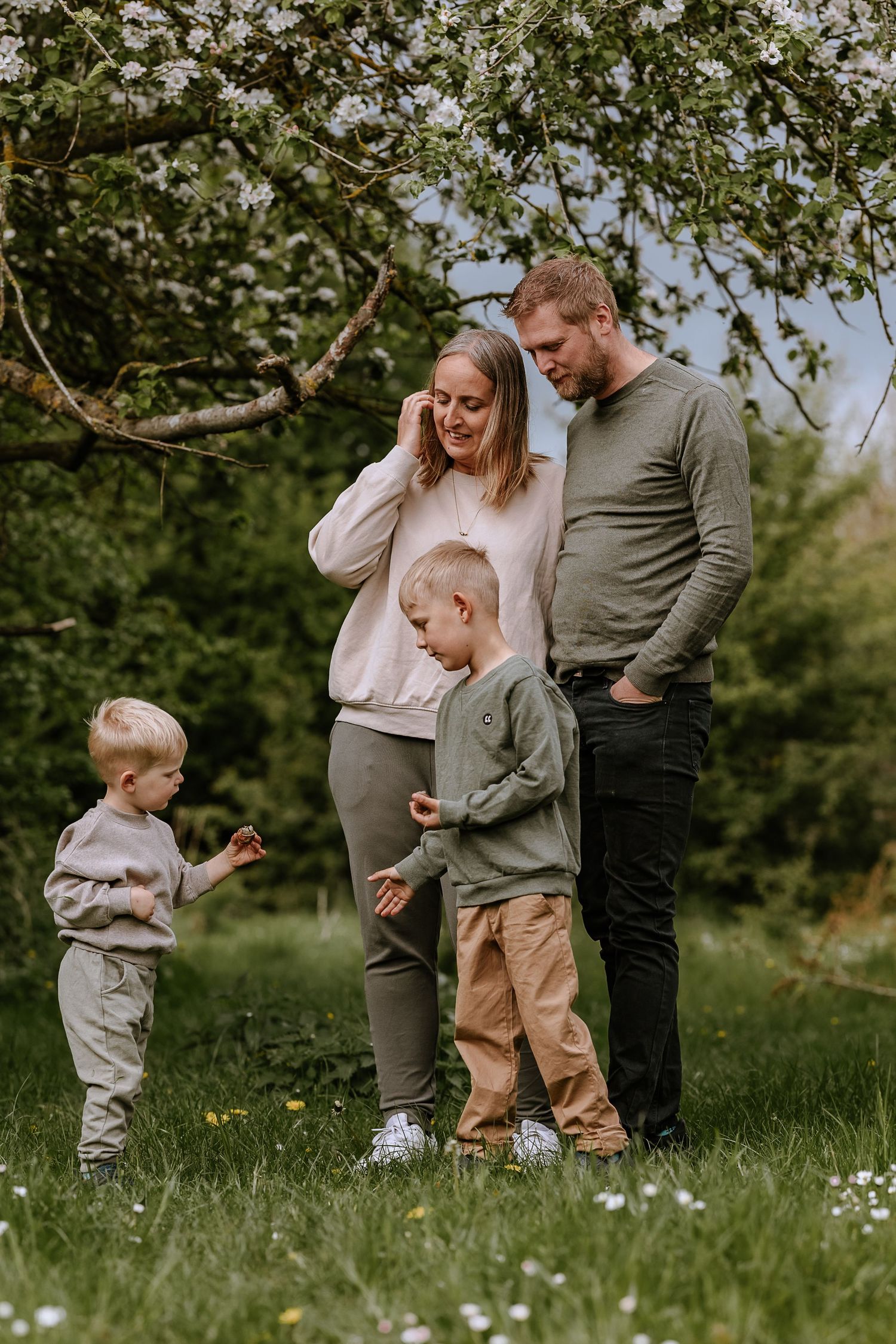 A family enjoys a spring day together under flowering trees in a grassy meadow.