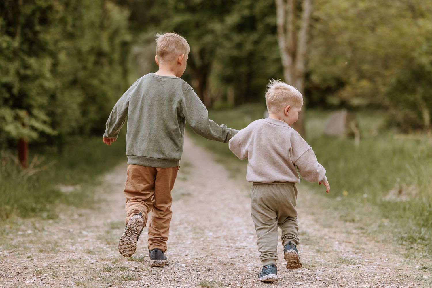 Two young children walking hand in hand down a dirt path surrounded by nature.