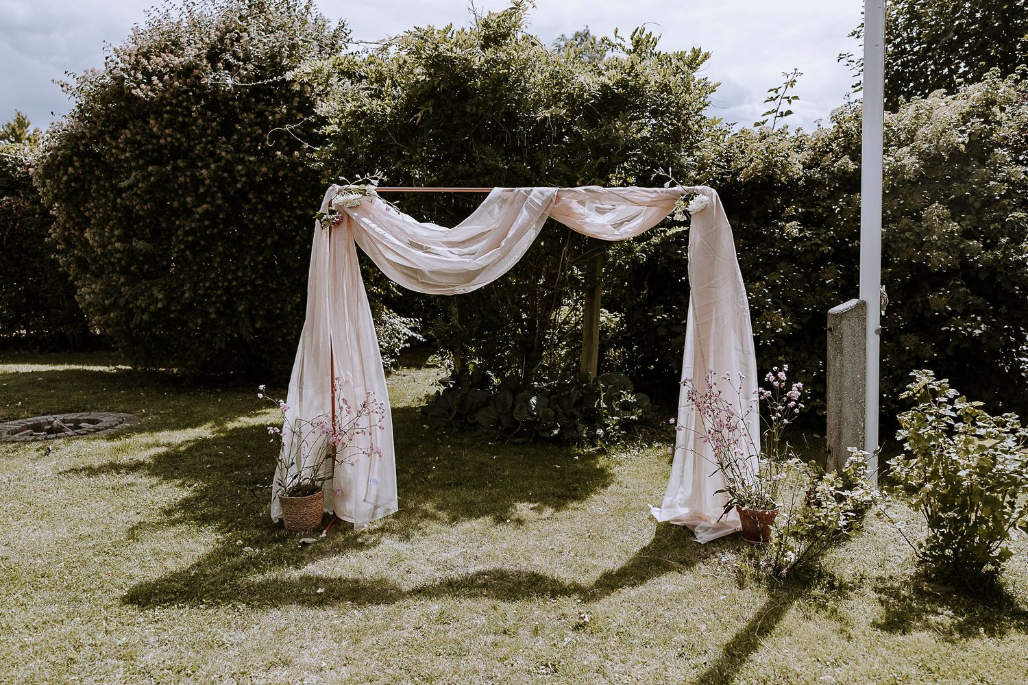 White fabric draped wedding arch set up in garden with natural greenery backdrop.