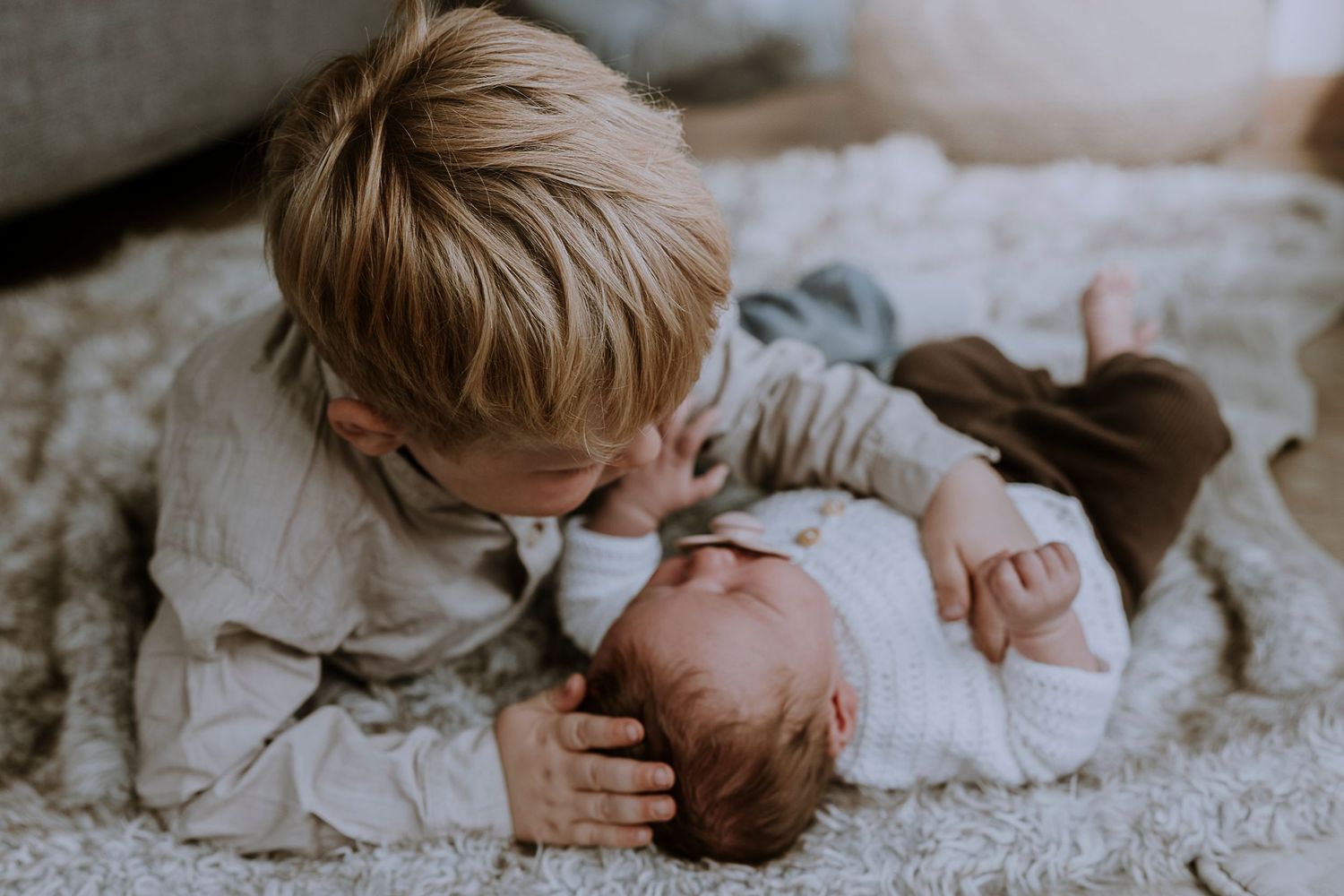 Two siblings share a sweet moment together on a cozy blanket.