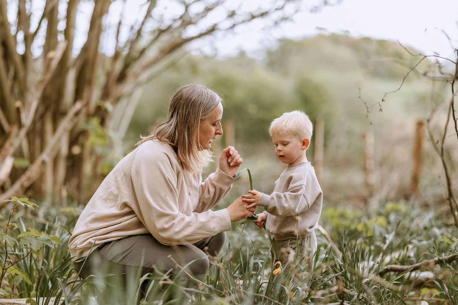 Parent and child share intimate moment examining flowers in natural setting.