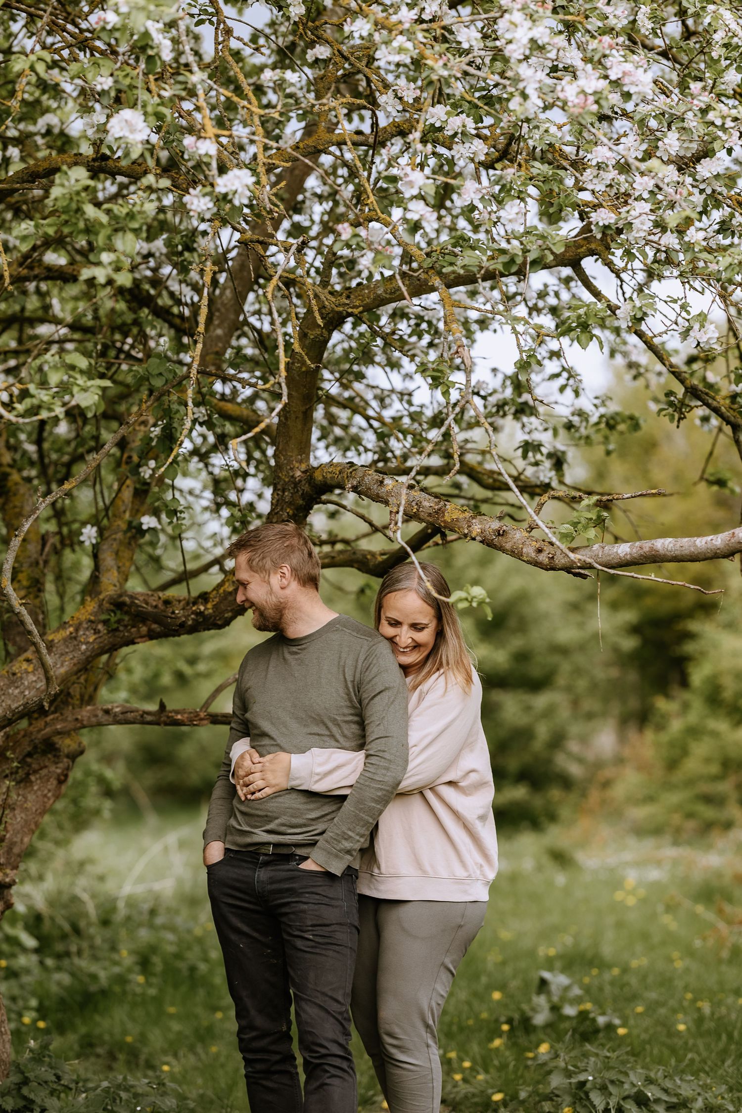 Couple sharing tender moment under flowering tree in natural outdoor setting.