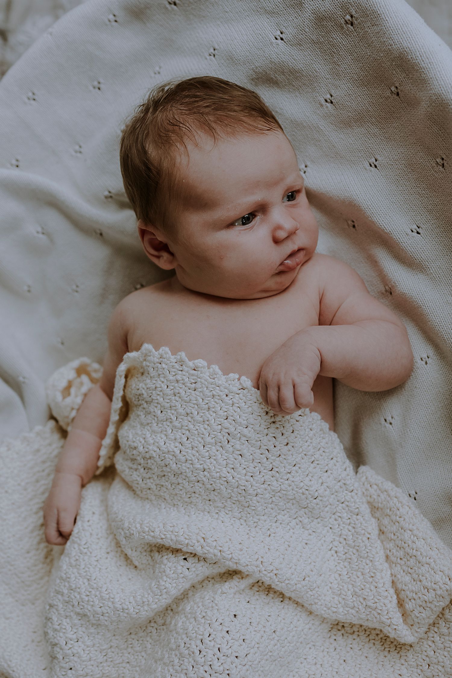 A newborn baby wrapped in a white textured blanket while resting on a soft surface.