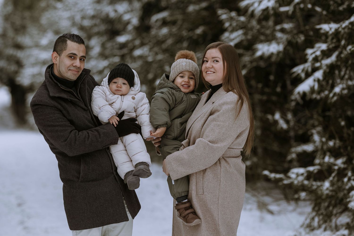 A group enjoys a winter photoshoot in the snow surrounded by evergreen trees.