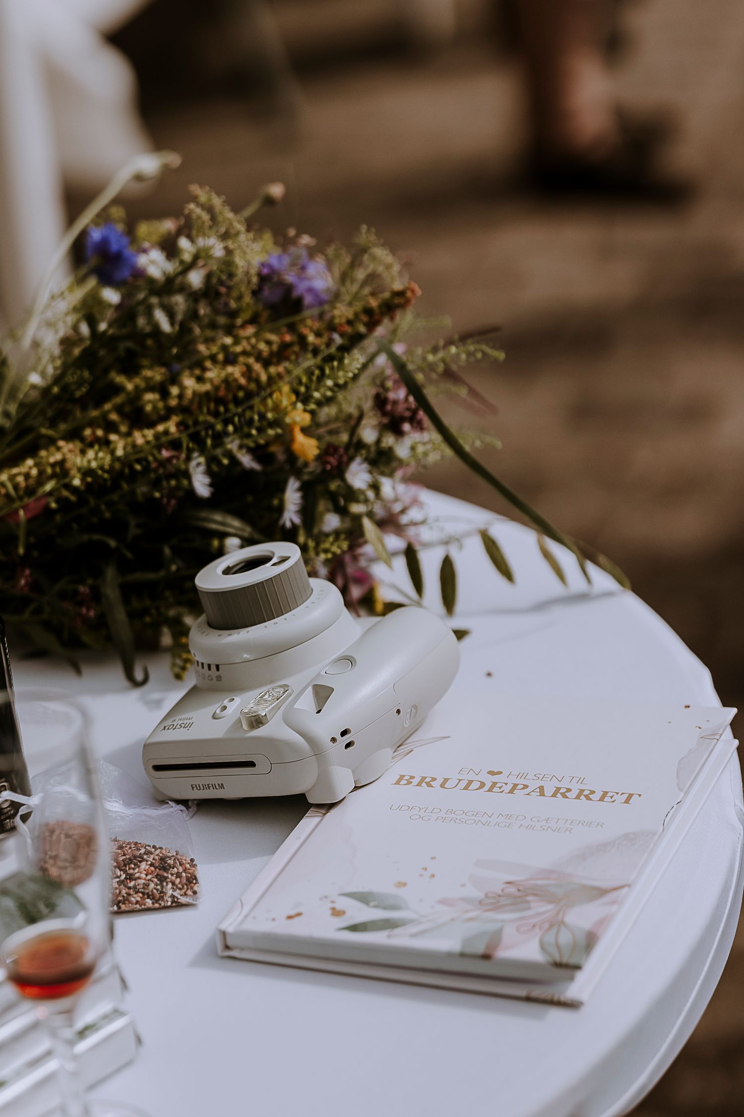 Wedding details on white table with instant camera and floral arrangements.