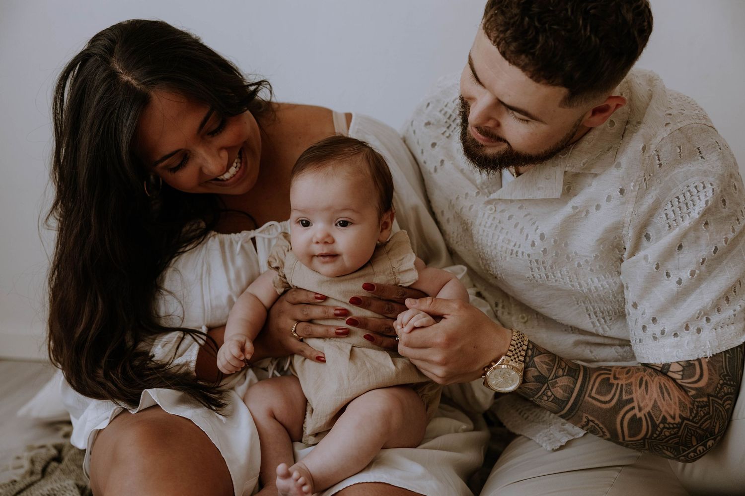 A loving family snuggles together on a white surface in an intimate indoor portrait.