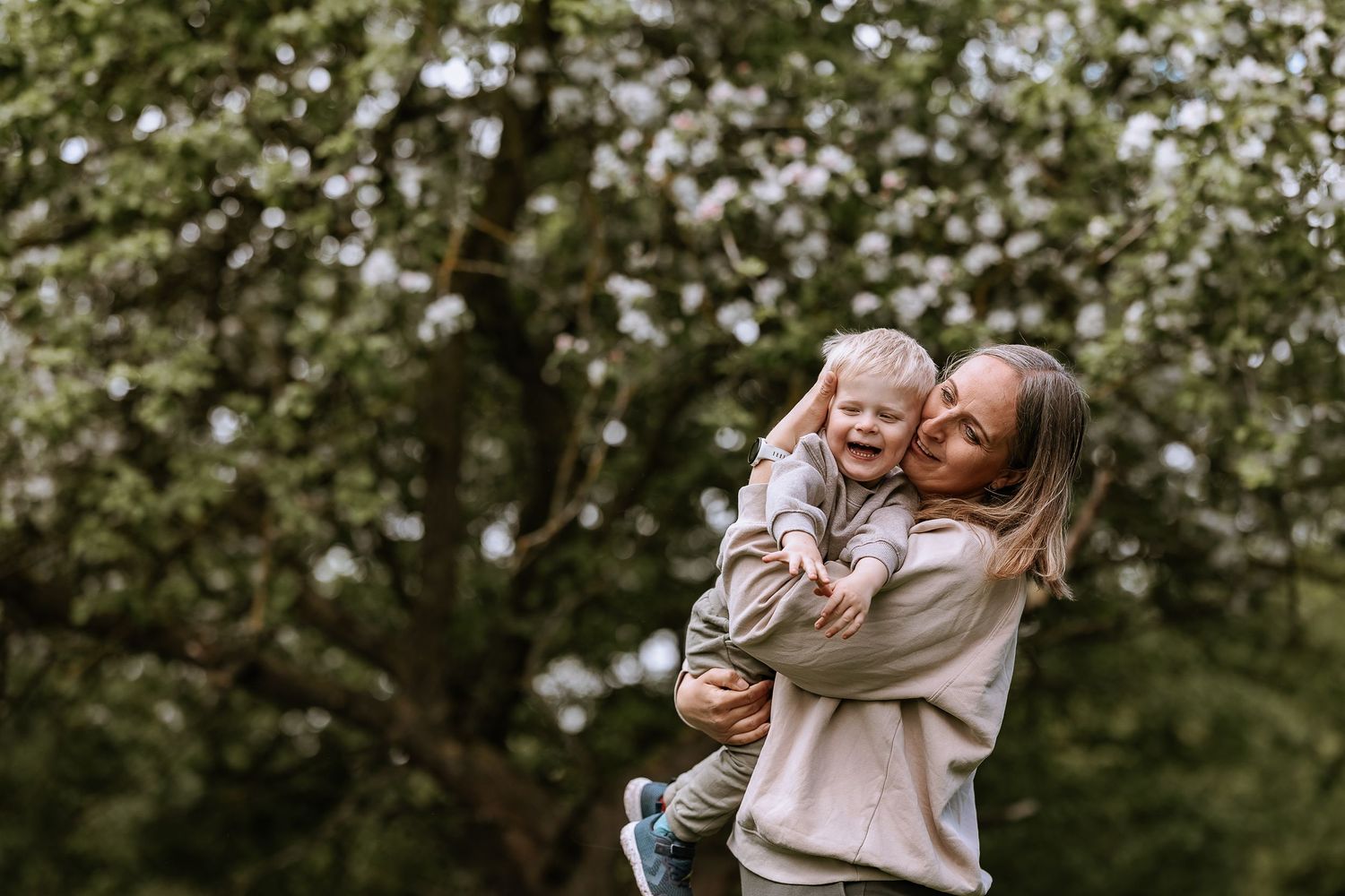 A tender embrace shared between parent and child amid blooming trees in a natural outdoor setting.