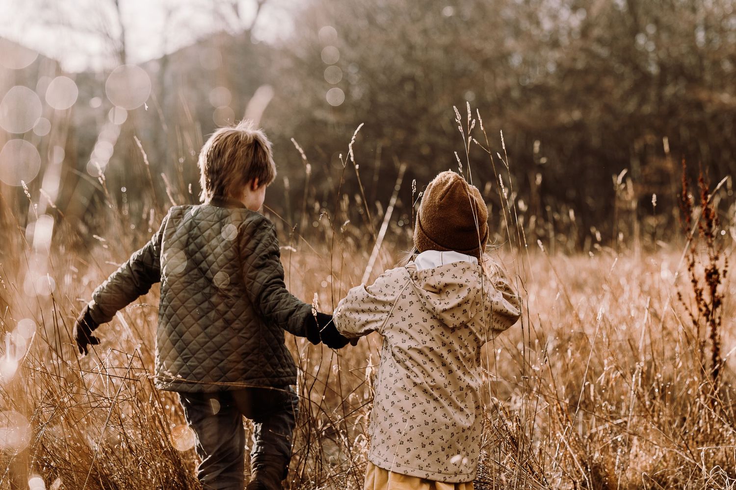 A sepia-toned collage of people walking through tall grass and wildflowers in a rustic outdoor setting.