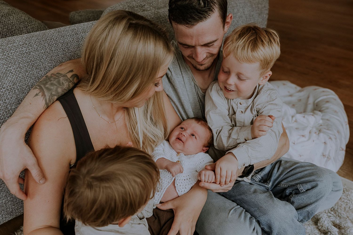 Family cuddles together on couch while meeting their newest member.
