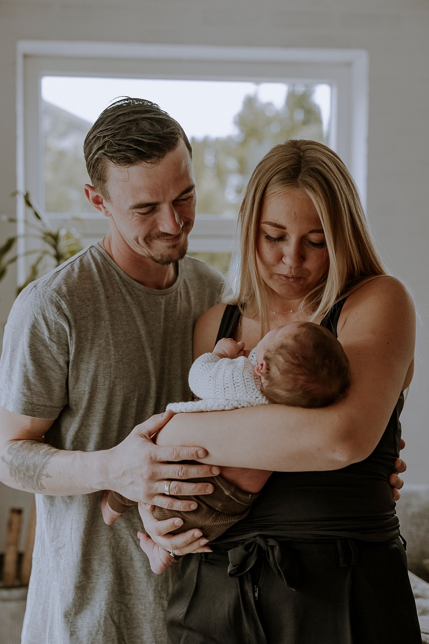 Couple tenderly embracing their newborn baby in a bright sunlit room.