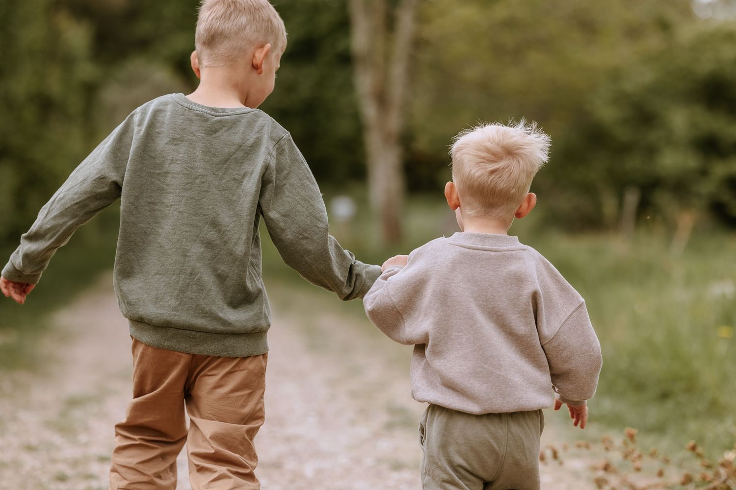 Two children walking together on a nature path wearing casual sweaters.