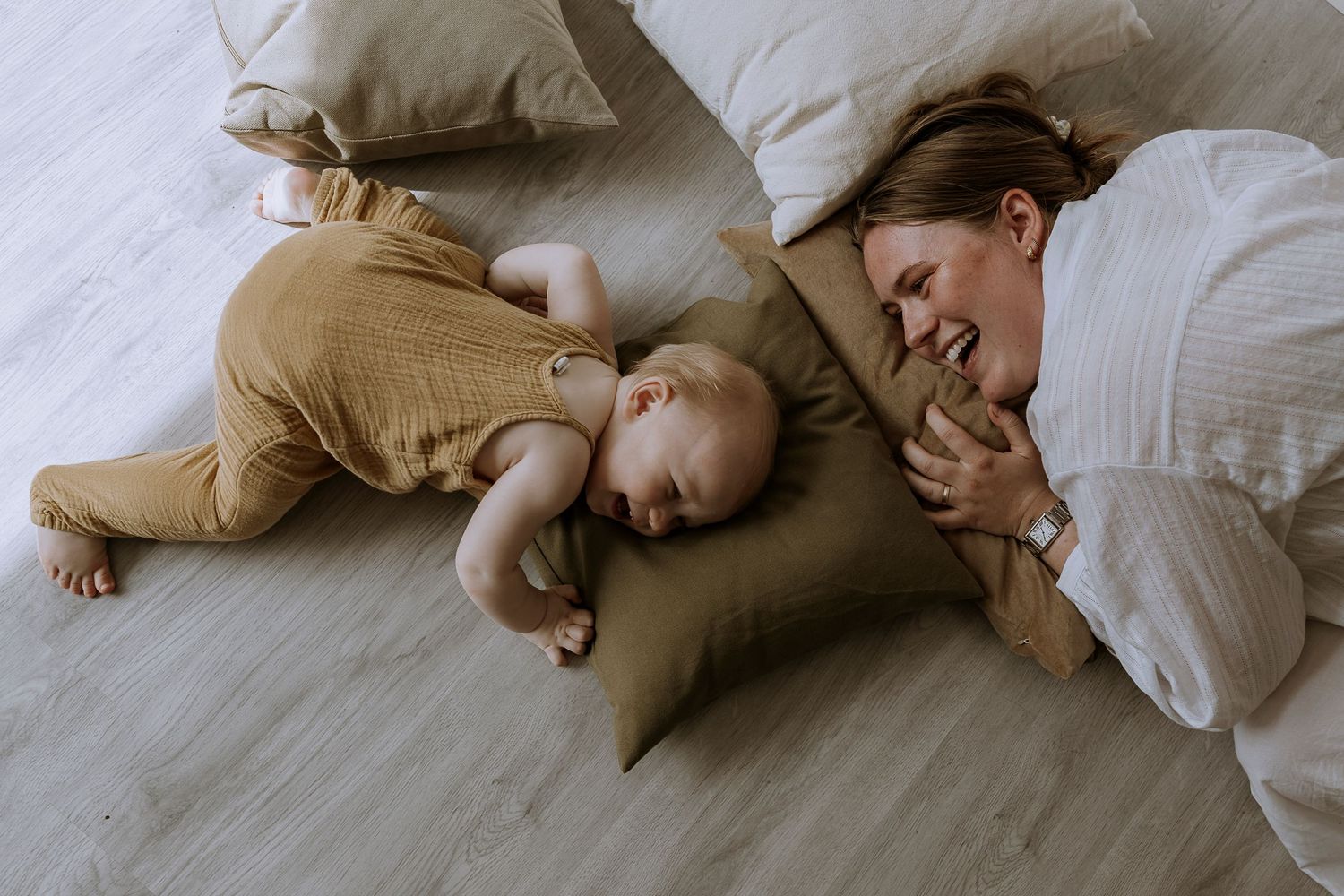 Parent and baby lying on floor sharing playful moment together near pillow.