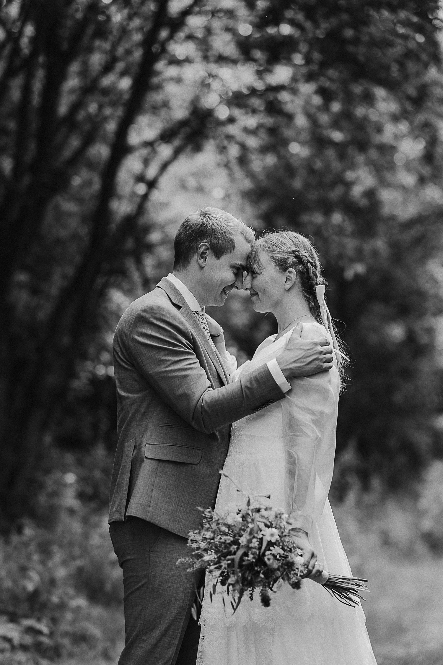 Black and white wedding portrait showing an intimate embrace with the bride holding a rustic bouquet.