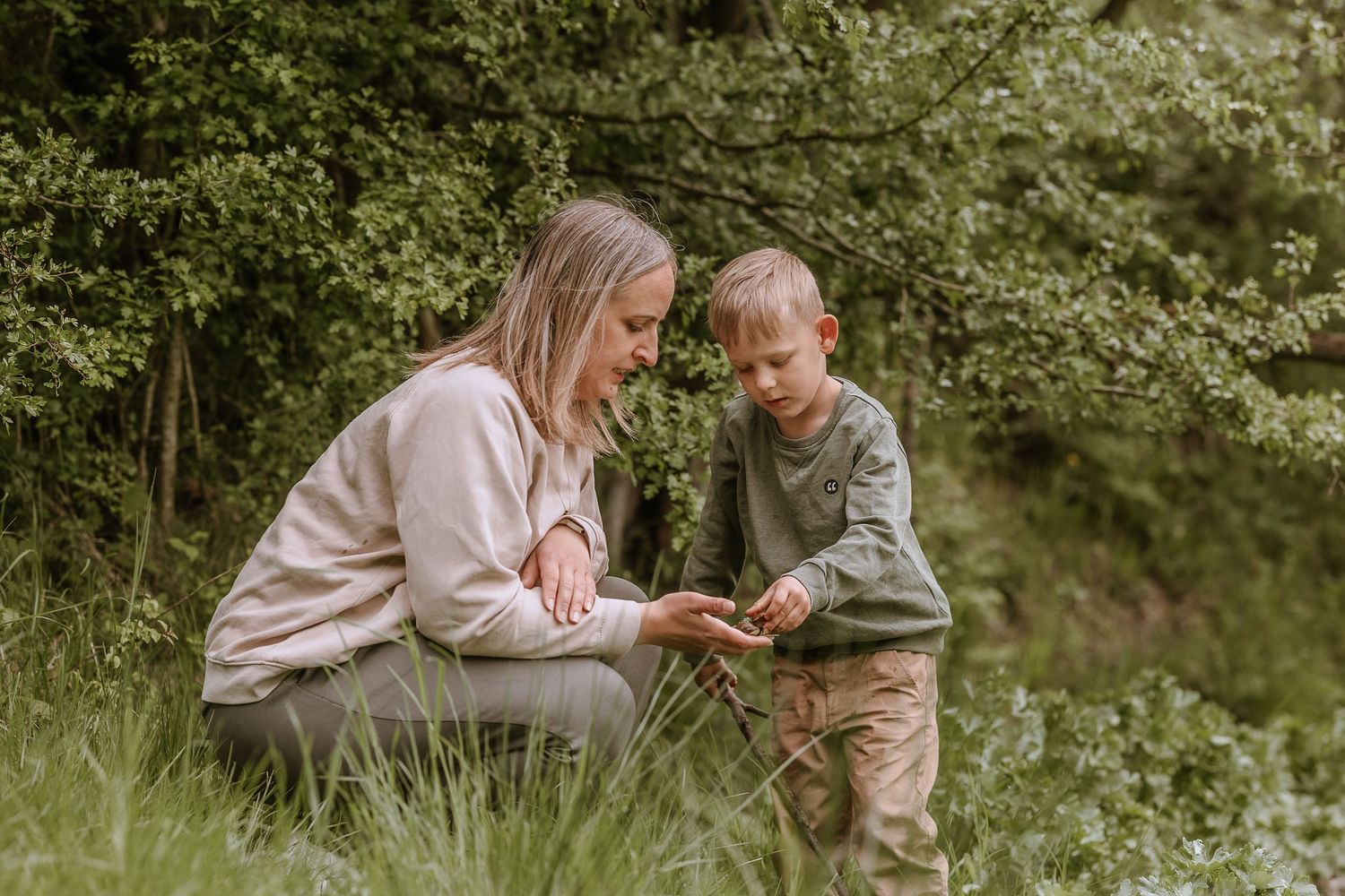 A tender interaction between two people sitting in tall grass with green foliage in the background.