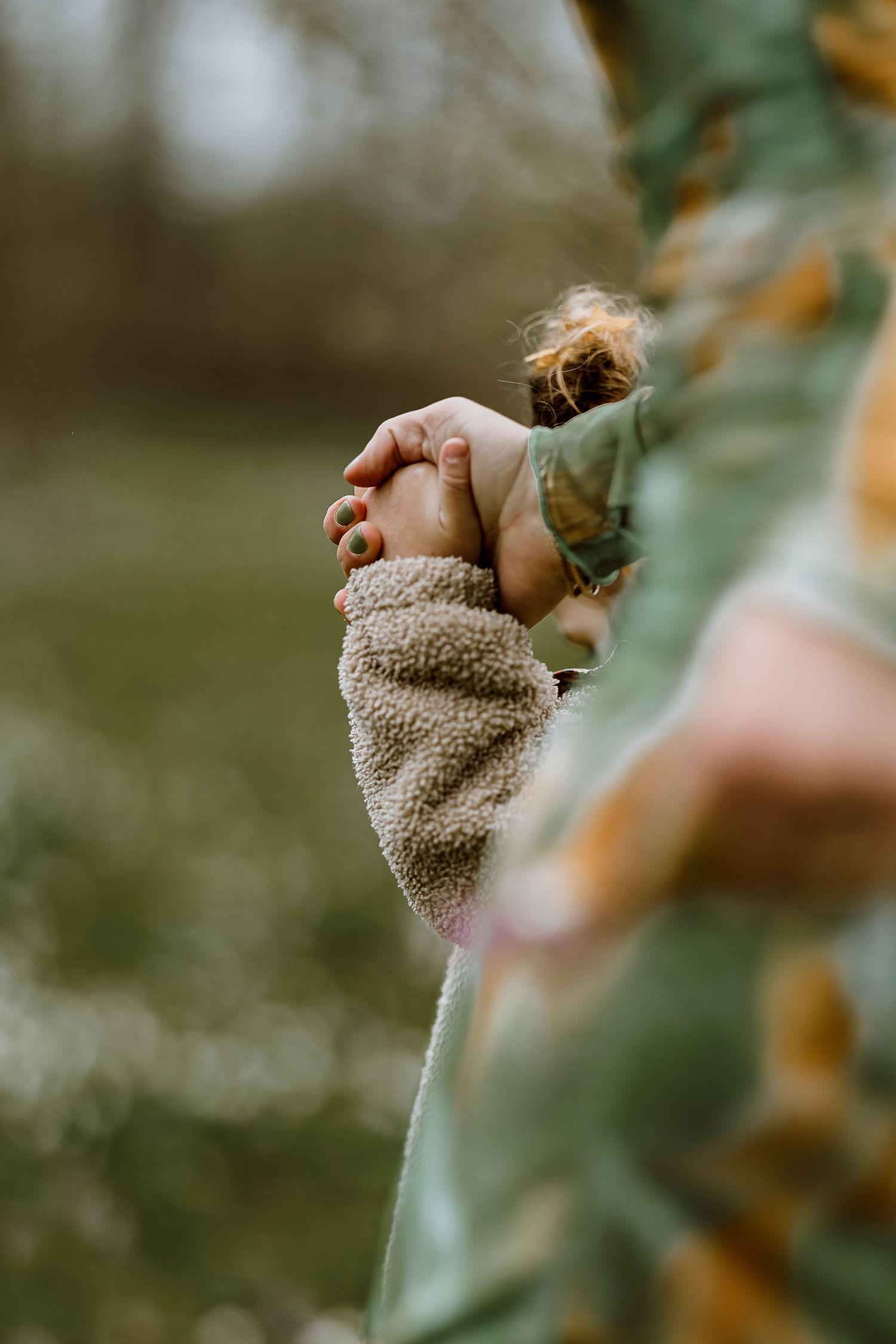 A small hand reaches out from a cozy beige sweater against a soft blurry natural background.