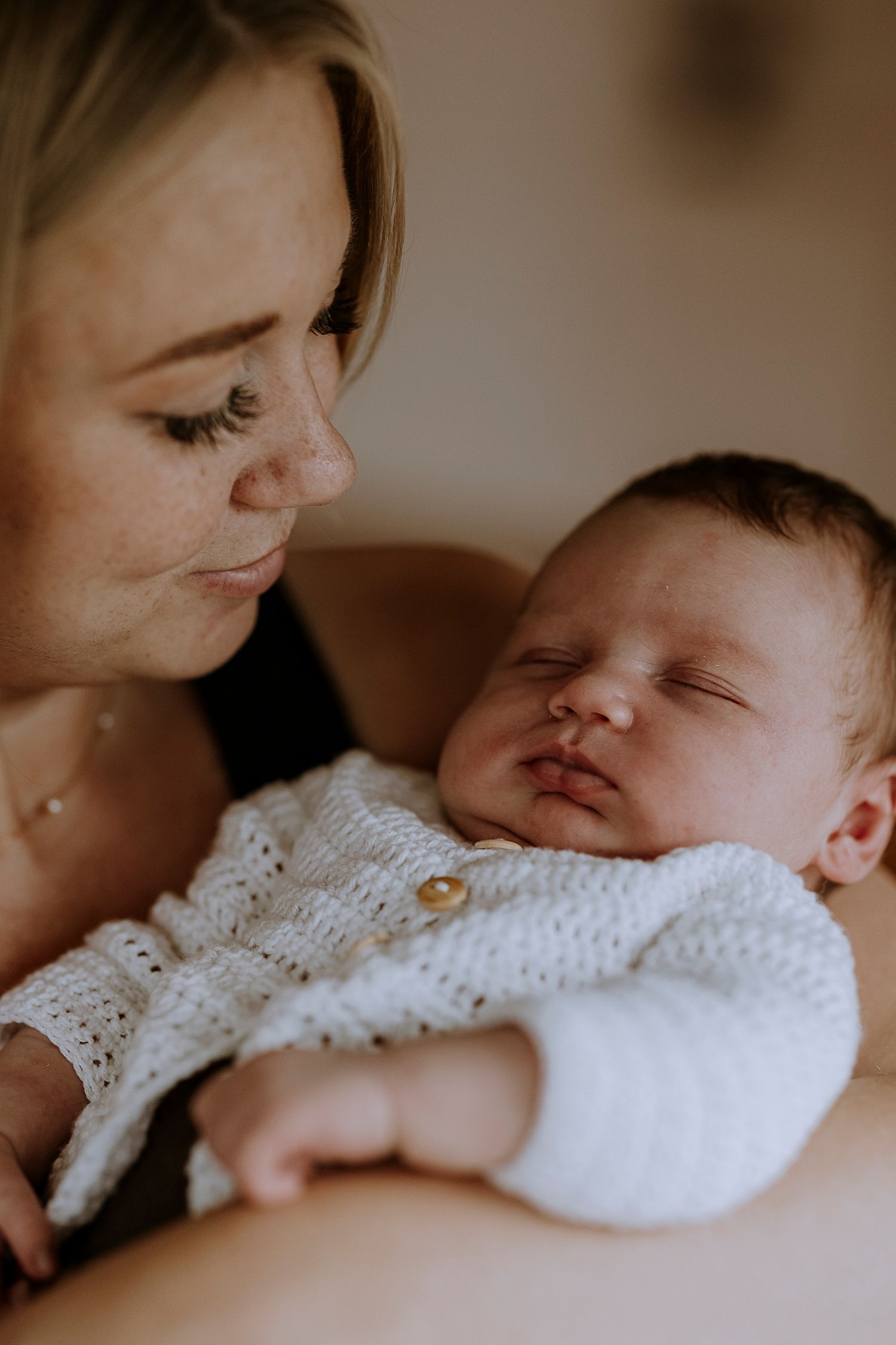 Parent gazing lovingly at sleeping newborn wearing white knit clothing.
